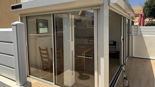 A glass-enclosed patio with a sliding door, a wooden table, and chairs.