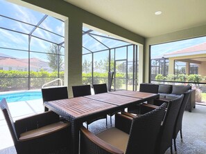 A covered patio area with a pool, outdoor seating, and large windows offering views of the surrounding area.