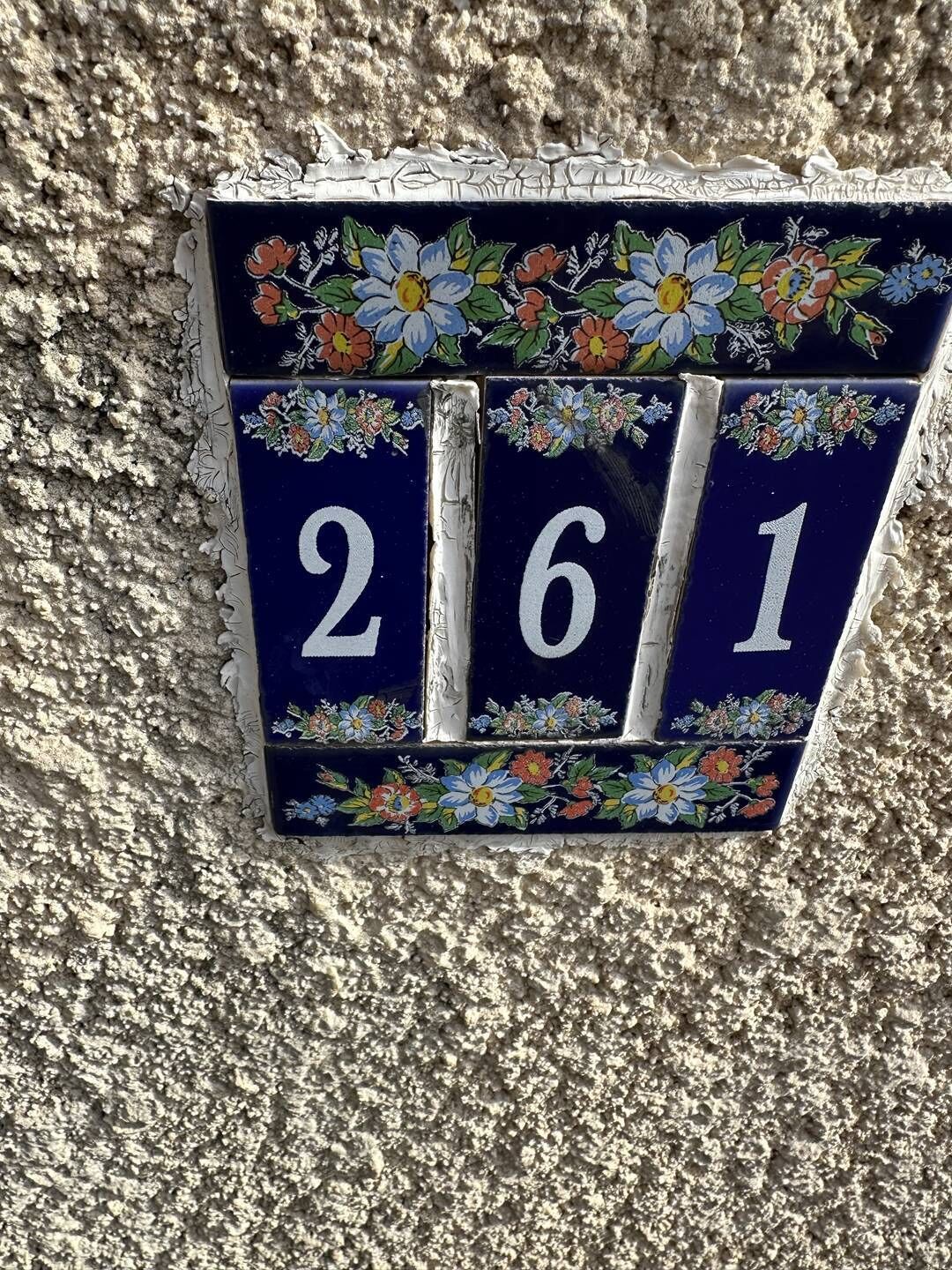 Une plaque de numéro de maison ornée de motifs floraux et portant le numéro 261.