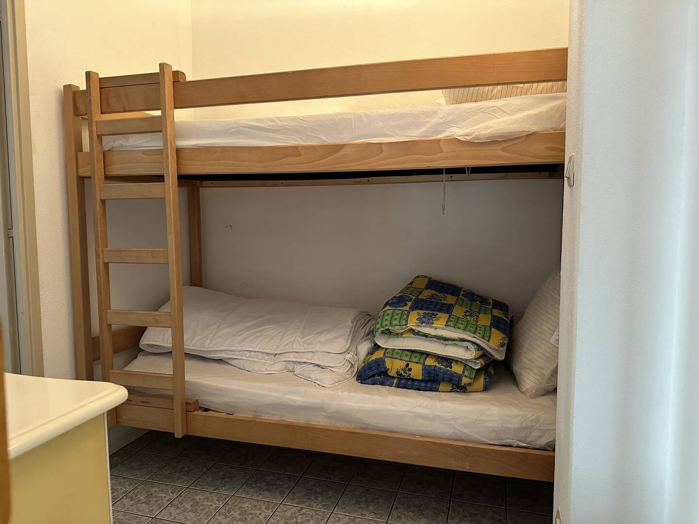 Una cama litera con escalera de madera, un colchón blanco y una colcha colorida.