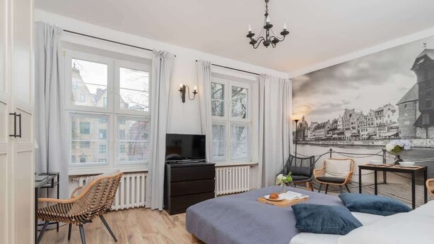Une chambre d’hôtel moderne dotée d’un grand lit, d’un bureau avec une chaise, d’une télévision et offrant une vue sur le paysage urbain par les fenêtres.