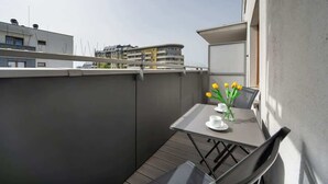 En balkon med et bord, stole og en vase med gule blomster.