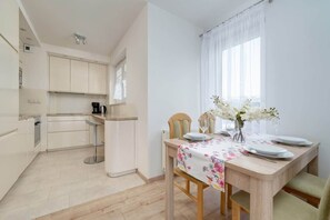 A modern kitchen with white cabinets, a dining table set with white plates, and a vase with flowers. - Functional Apartment | Parking, Balcony, Close to Park (Wroclaw)