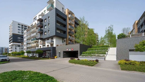 En moderne lejlighedsbygning med flere altaner, en lukket indgang og en anlagt have.