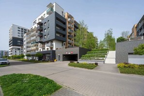 Un moderno edificio de apartamentos con varios balcones, entrada protegida por un portón y un jardín ajardinado.