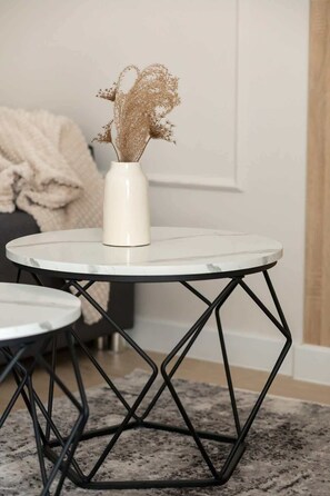 A round white table with a white vase containing dried flowers, set on a black metal base.