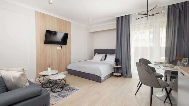 Moderni hotellihuone, jossa on sänky, televisio, ruokailutila ja suuri ikkuna, jossa on verhot.