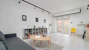 A modern living room with a grey sofa, a round wooden coffee table, a bookshelf, and a bright yellow chair. - Comfortable Apartment | Balcony, Workspace, High Speed WiFi (Łódź)