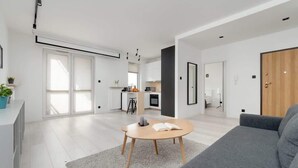 A modern living room with a grey sofa, a round coffee table, and a kitchen in the background. - Comfortable Apartment | Balcony, Workspace, High Speed WiFi (Łódź)