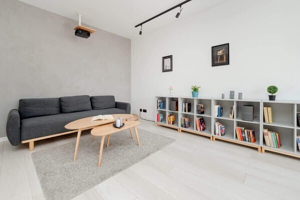 A modern living room with a grey sofa, a wooden coffee table, a bookshelf, and a grey rug. - Comfortable Apartment | Balcony, Workspace, High Speed WiFi (Łódź)
