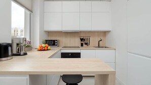 A modern kitchen with white cabinets, a wooden countertop, a coffee maker, a microwave, and a fruit bowl. - Comfortable Apartment | Balcony, Workspace, High Speed WiFi (Łódź)