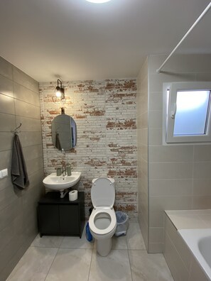 A compact bathroom with a modern design, featuring a white toilet, sink, and cabinet, set against a rustic brick-patterned wall.