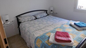A small, simple bedroom with a bed, a bedside table with a lamp, and a window. - HOLIDAYLAND T2 MEZZANINE 314 6 beds NARBONNE PLAGE (NARBONNE PLAGE)