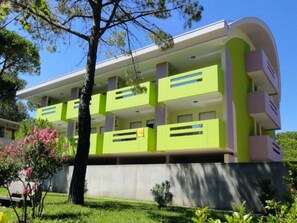 Un immeuble moderne à plusieurs étages, doté de balcons et entouré de verdure et d’arbres.