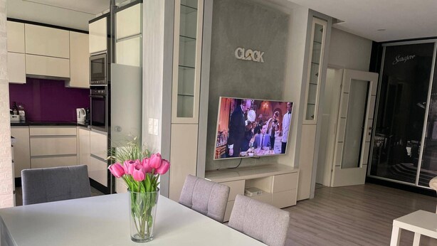 A modern living room with a flat-screen TV, a dining table with chairs, and a vase of flowers. - Beautiful 2-bed Apartment in Wien (Vienna)