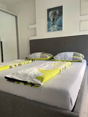 Ett hotellrum med en stor säng, ett grått sänggavel och en affisch som föreställer en person på en månbelyst strand.