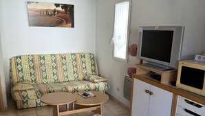 Un petit salon avec un canapé, un téléviseur, un meuble et une table.