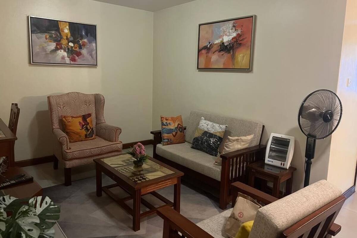 A living room with a sofa, armchairs, a coffee table, and a fan.