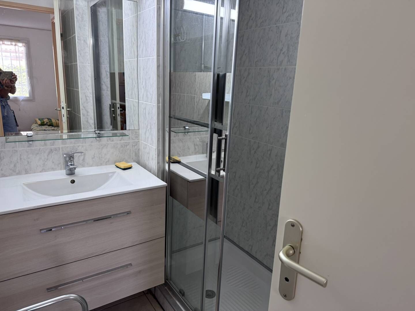 Un bany modern amb plat de dutxa de vidre, un lavabo blanc i un mirall gran.