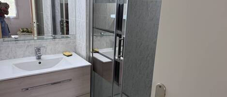 Un bany modern amb plat de dutxa de vidre, un lavabo blanc i un mirall gran.