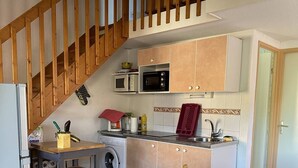 Une cuisine compacte avec un escalier en bois, un lave-linge, un four à micro-ondes et un coin repas comprenant une table et des chaises.
