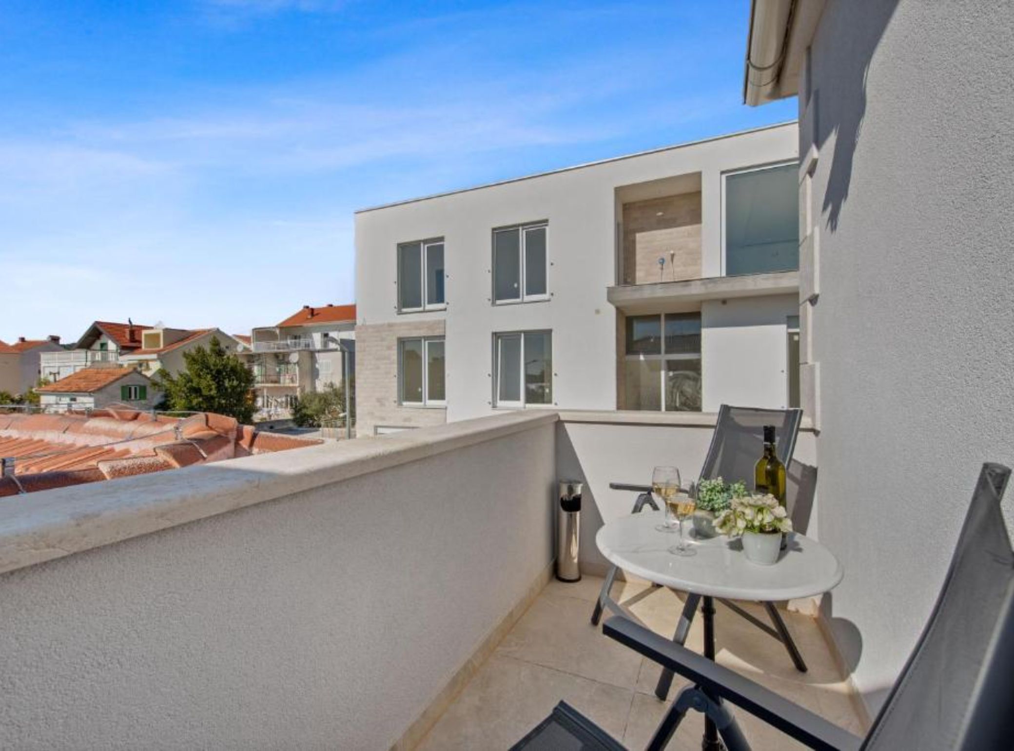 Ein Balkon mit einem Tisch für zwei Personen, einer Weinflasche und einer Blumenkomposition.