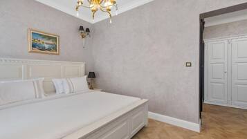 A bedroom with a large bed, a chandelier, a painting on the wall, and a door to the right.