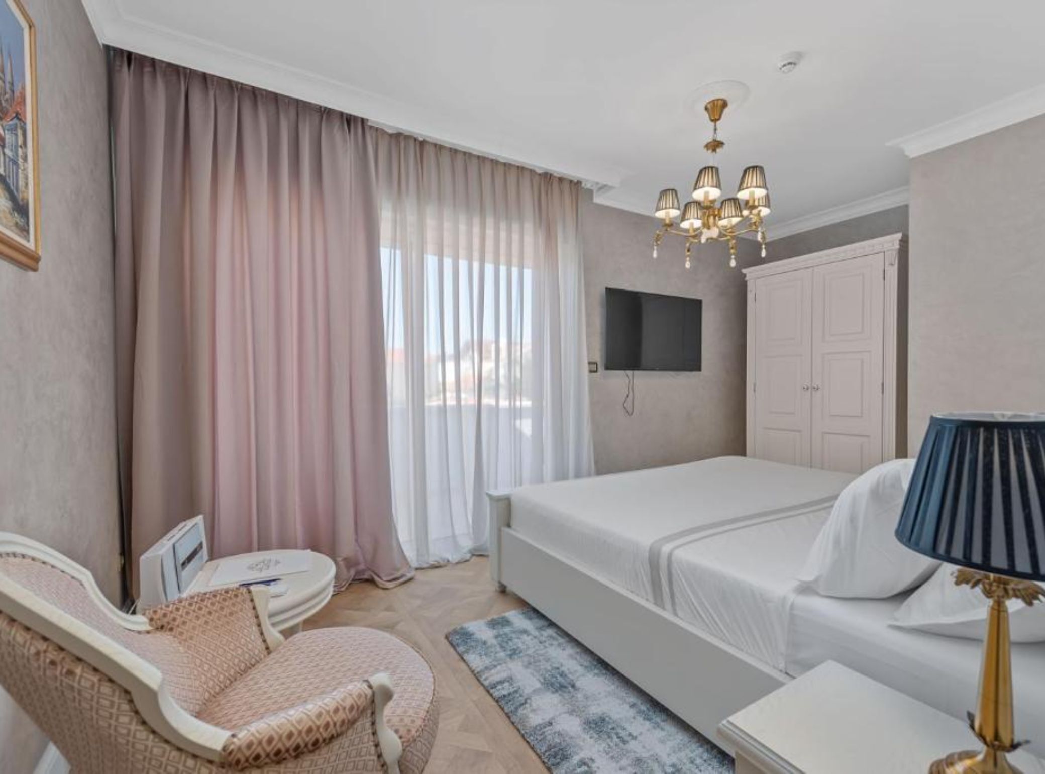 A bedroom with a bed, a TV mounted on the wall, a wardrobe, a chair, and a lamp.