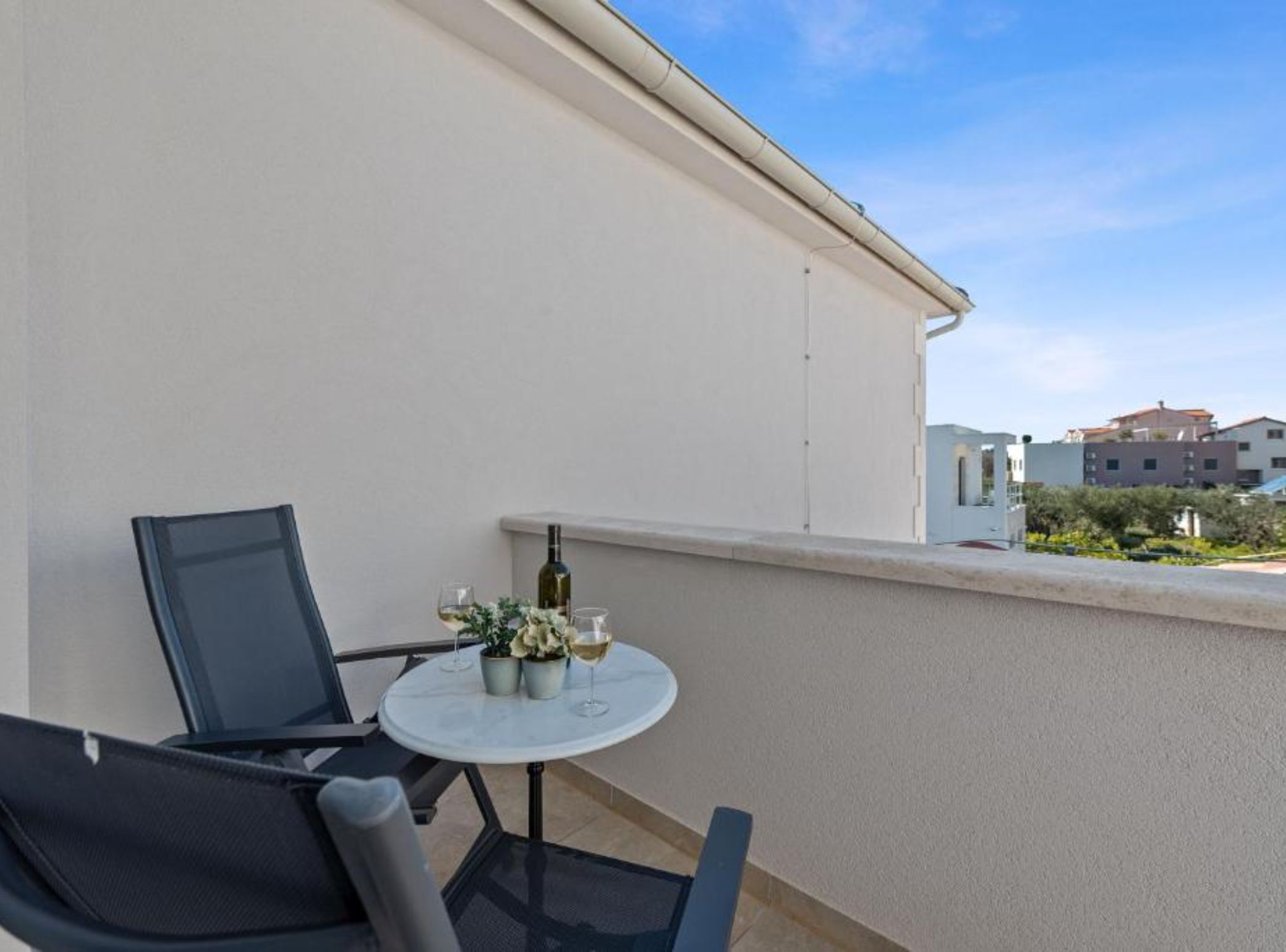 A balcony with a round table, two chairs, a bottle of wine, and a small plant.