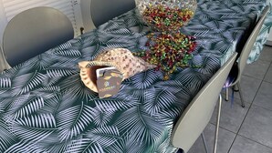 A dining table with a tropical leaf pattern tablecloth, a decorative glass bowl with colorful ornaments, and a card game on the table.
