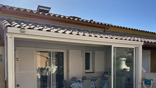 A covered patio with a table and chairs, a sliding glass door, and a water hose.