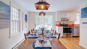 A dining area with a wooden table set for six, a hanging pendant light, and a kitchen with stainless steel appliances. - Private Lake Access, Great for Families! (Orleans)