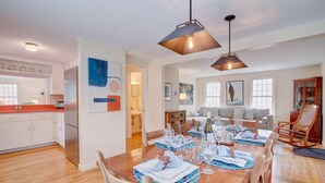 A dining area with a wooden table set for six, a kitchen with white cabinets, and a living room with a sofa and a large window. - Private Lake Access, Great for Families! (Orleans)