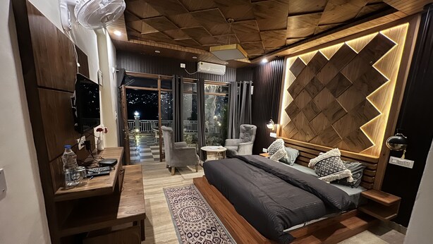 A modern bedroom with a large bed, a desk, and a chair. There is a balcony with a view of the city at night. - House of lights - Solan  (Solan)