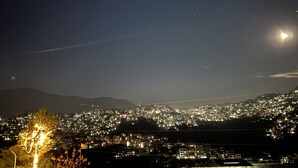 A nighttime cityscape with a prominent hill in the background and a visible contrail in the sky. - House of lights - Solan  (Solan)