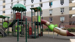 Ein Spielplatz mit Rutsche und Klettergerüsten, umgeben von einem Gebäude mit vielen Fenstern.