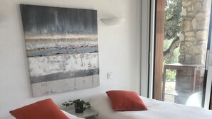 Une chambre avec deux lits, un tableau accroché au mur et une vue sur l’extérieur, visible à travers une porte vitrée.