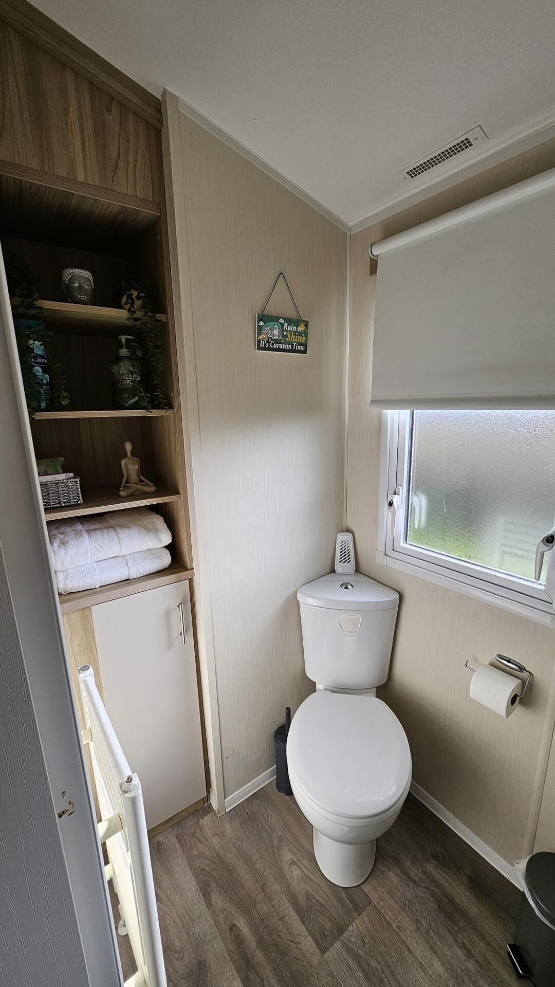 A compact bathroom with a toilet, a shelf with toiletries, and a small window.