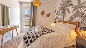 A bedroom with a bed, a desk, a lamp, and a wall with palm tree artwork. - Rivages Appartement Pleine vue mer Terrasse Privative et Garage (Brest)