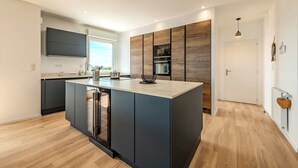 A modern kitchen with a central island, built-in appliances, and a large window. - Rivages Appartement Pleine vue mer Terrasse Privative et Garage (Brest)