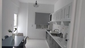 A modern kitchen with white cabinets, a dining table with chairs, and a pendant light. - Samos Home by the sea (Samos)