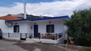 A white building with blue trim, a covered patio with outdoor furniture, and a mountain backdrop. - Evdokia s Samos Home (Samos)