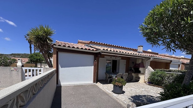 A residential property with a closed garage, a patio with outdoor furniture, and a small garden area.