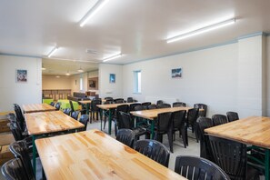 Classroom or meeting room with long tables and black chairs, framed pictures on the walls, and a window.