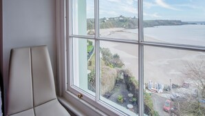 A room with a large window overlooking a beach, a chair, and some outdoor furniture.