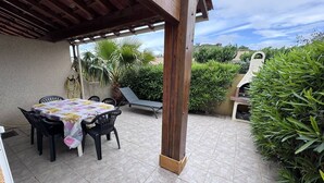 En uteplats med ett bord och stolar, en grill och frodig grönska.