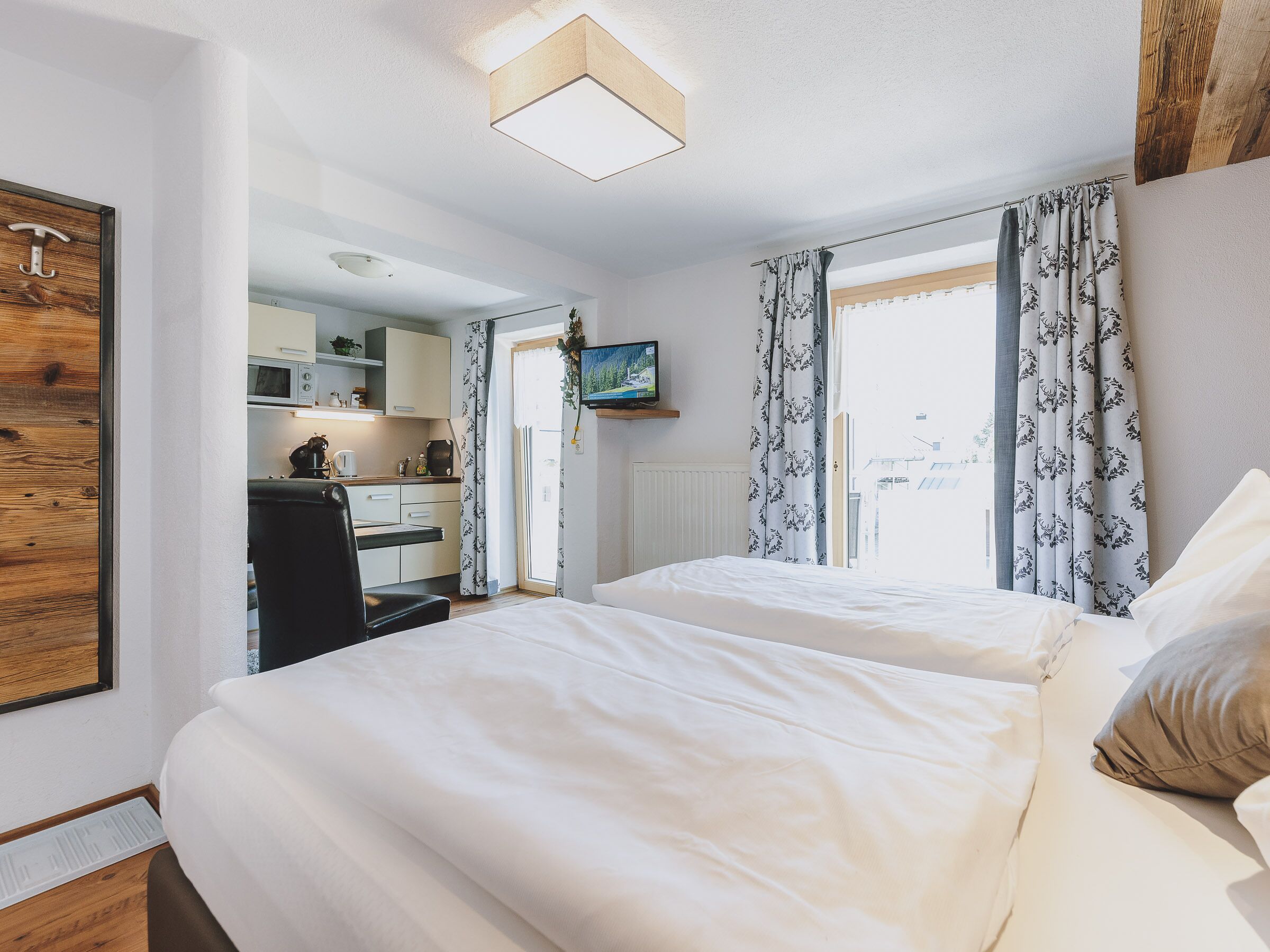 A bedroom with two beds, a desk, and a kitchenette.