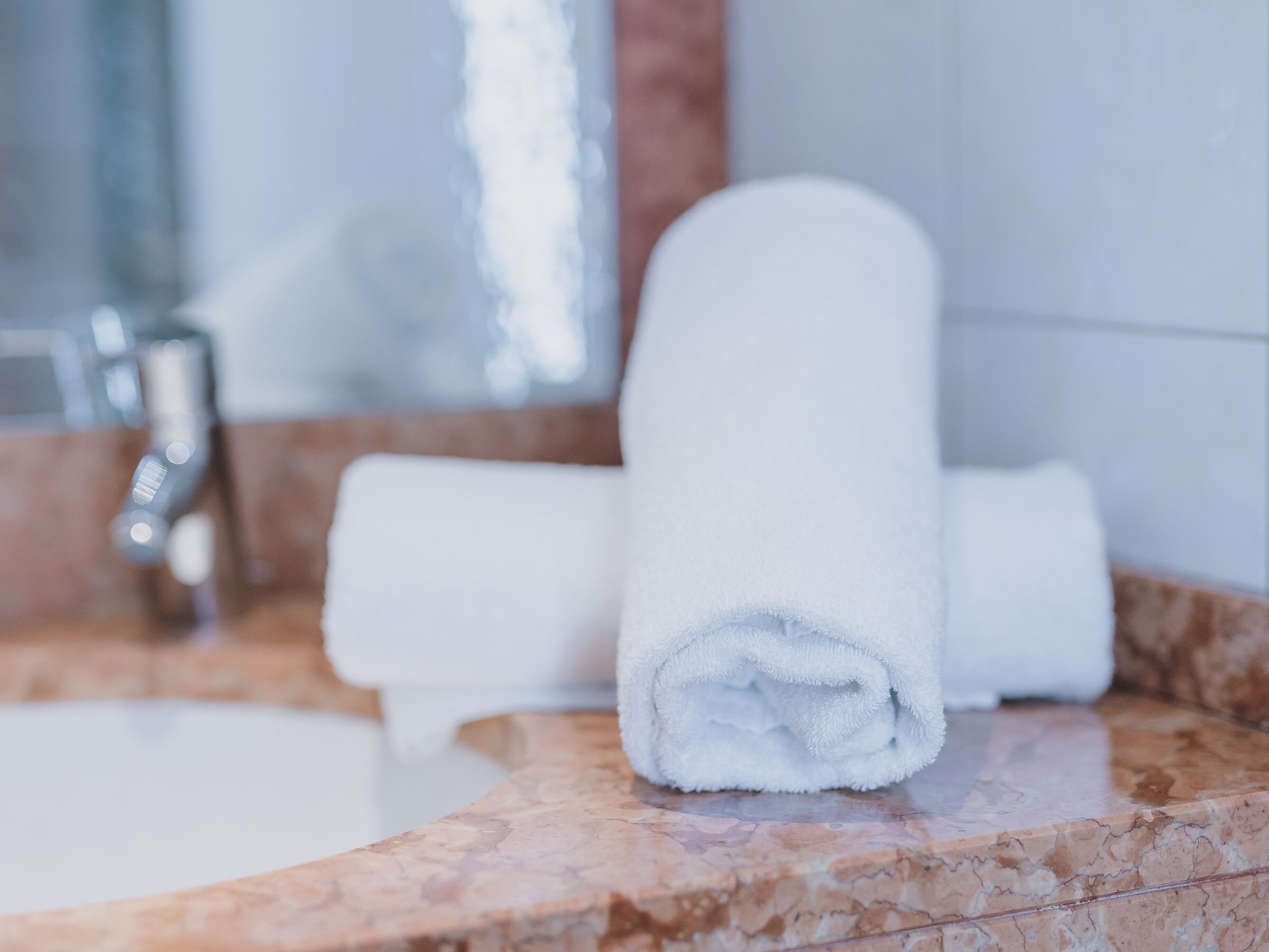 Une salle de bain avec un comptoir en marbre, une serviette blanche et un robinet moderne.