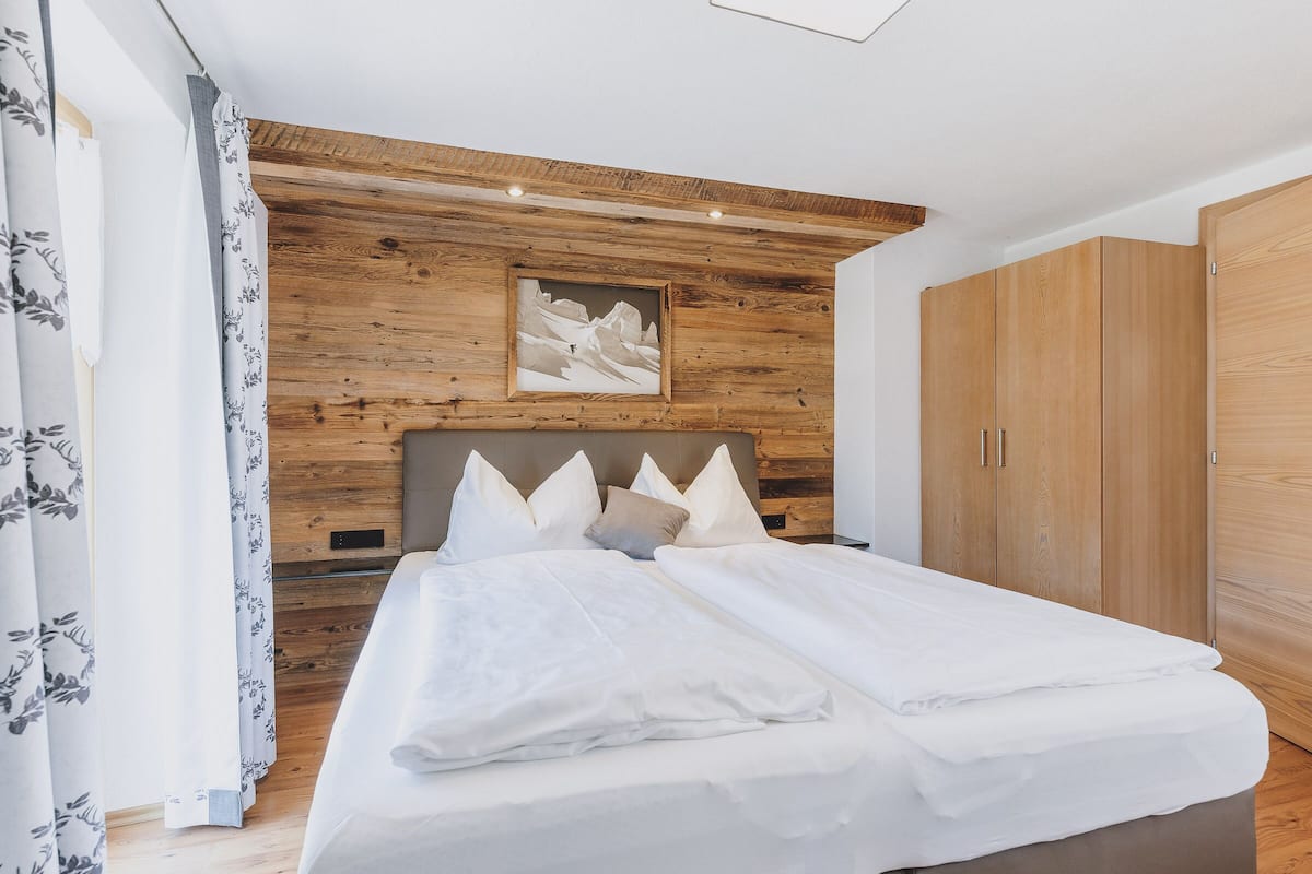 A bedroom with a wooden headboard, a bed with white linens, a wooden wardrobe, and a painting on the wall.