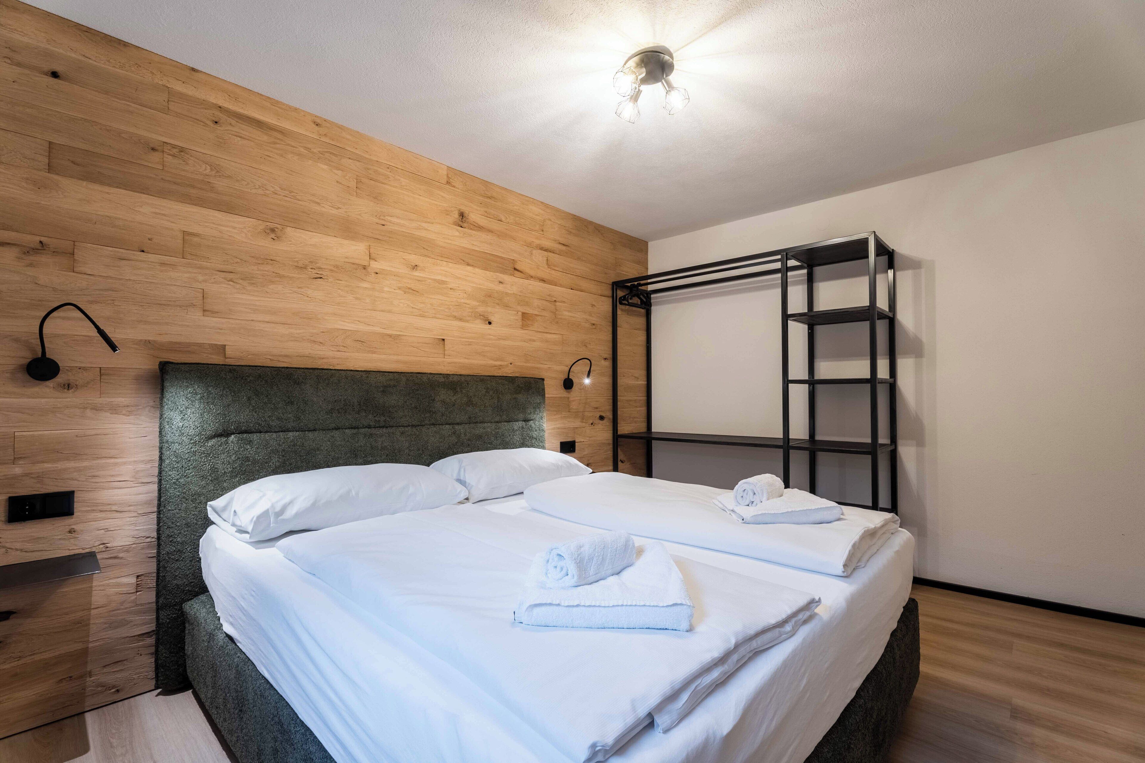 A hotel room with a wooden headboard, a bunk bed, a small shelf, and a wall-mounted light fixture.
